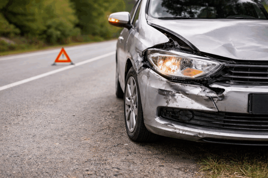 Beschädigtes Auto mit Frontschaden und Warndreieck nach einem Verkehrsunfall am Straßenrand